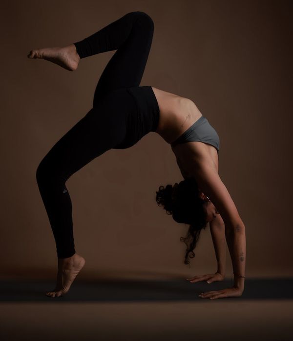 Young woman practicing balance yoga pose in a dark studio with cyan lighting.
